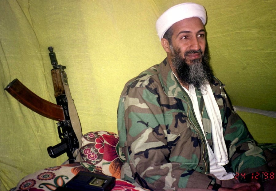 FILE - In this Dec. 24, 1998, file photo, al-Qaida leader Osama Bin Laden speaks to a selected group of reporters in mountains of Helmand province in southern Afghanistan. When the reclusive Islamic State group leader Abu Bakr al-Baghdadi appeared in a video Monday, he was the latest in a series of most-wanted figures, to use the medium to communicate with the outside world. Al-Baghdadi in his latest video mirrored a picture of Osama Bin Laden in his videos, sitting cross-legged with an assault rifle kept against the wall next to him.