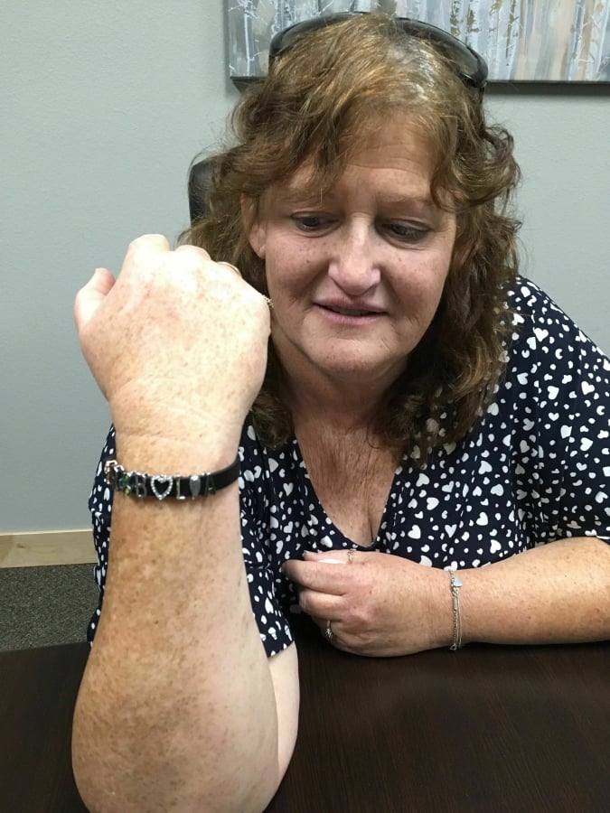 In this Monday, April, 15, 2019 photo, is Jackie Fakler, co-owner of RJR Maintenance and Management in Mandan, North Dakota, as she displays a wrist band someone sent her anonymously to show support after the slayings of four people at RJR on April 1, 2019. The dead included Fakler’s husband, Robert. The wrist band is ornamented with the first initials of the four victims, along with charms associated with each.