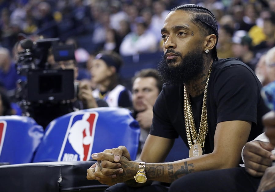 FILE - In this March 29, 2018, file photo, rapper Nipsey Hussle watches an NBA basketball game between the Golden State Warriors and the Milwaukee Bucks in Oakland, Calif. Grammy-nominated and widely respected West Coast rapper Nipsey Hussle has been shot and killed outside his Los Angeles clothing store, Los Angeles Mayor Eric Garcetti said Sunday, March 31, 2019. He was 33.