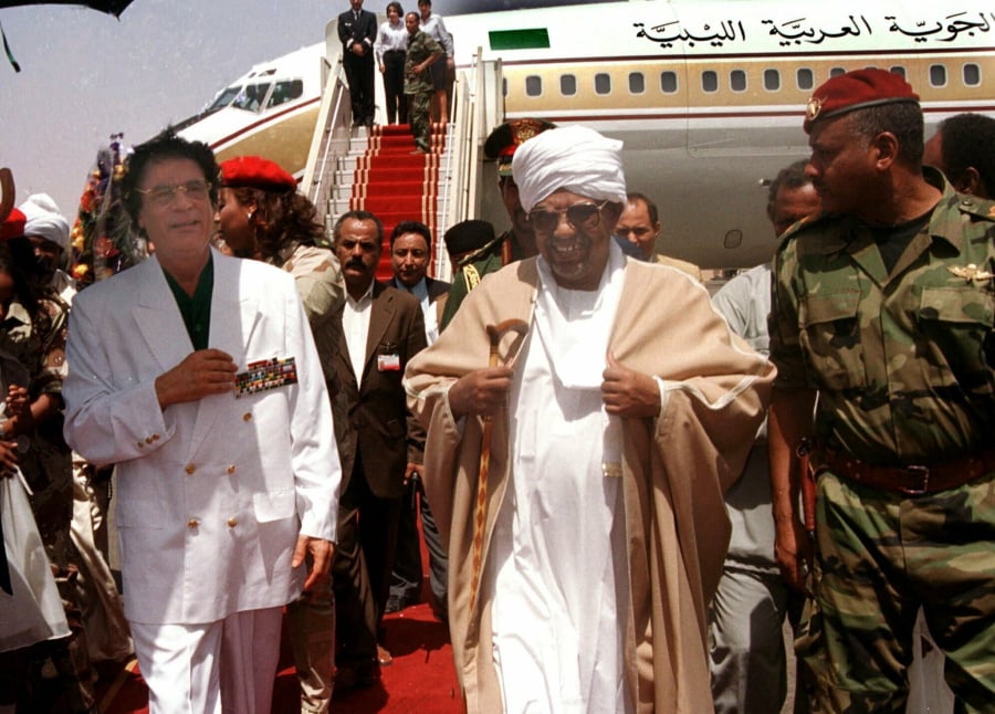 FILE - In this May 10, 2001, file photo, Libyan leader Moammar Gadhafi , left, is greeted by President Omar El-Bashir, center, upon his arrival in Khartoum for a two-day visit to Sudan. Tens of thousands of Sudanese were making their way to the center of the country’s capital on Thursday, April 11, 2019, cheering and clapping in celebration as two senior officials said the military had forced longtime autocratic President Omar al-Bashir to step down after 30 years in power.