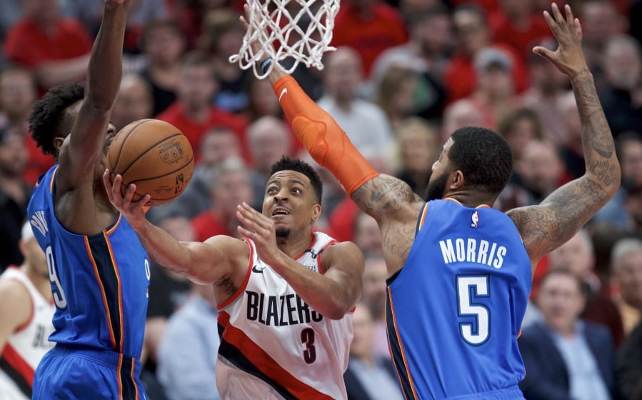 Portland Trail Blazers guard CJ McCollum, center, shoots between Oklahoma City Thunder forward Jerami Grant, left, and forward Markieff Morris during the second half of Game 2 of an NBA basketball first-round playoff series Tuesday, April 16, 2019, in Portland, Ore.