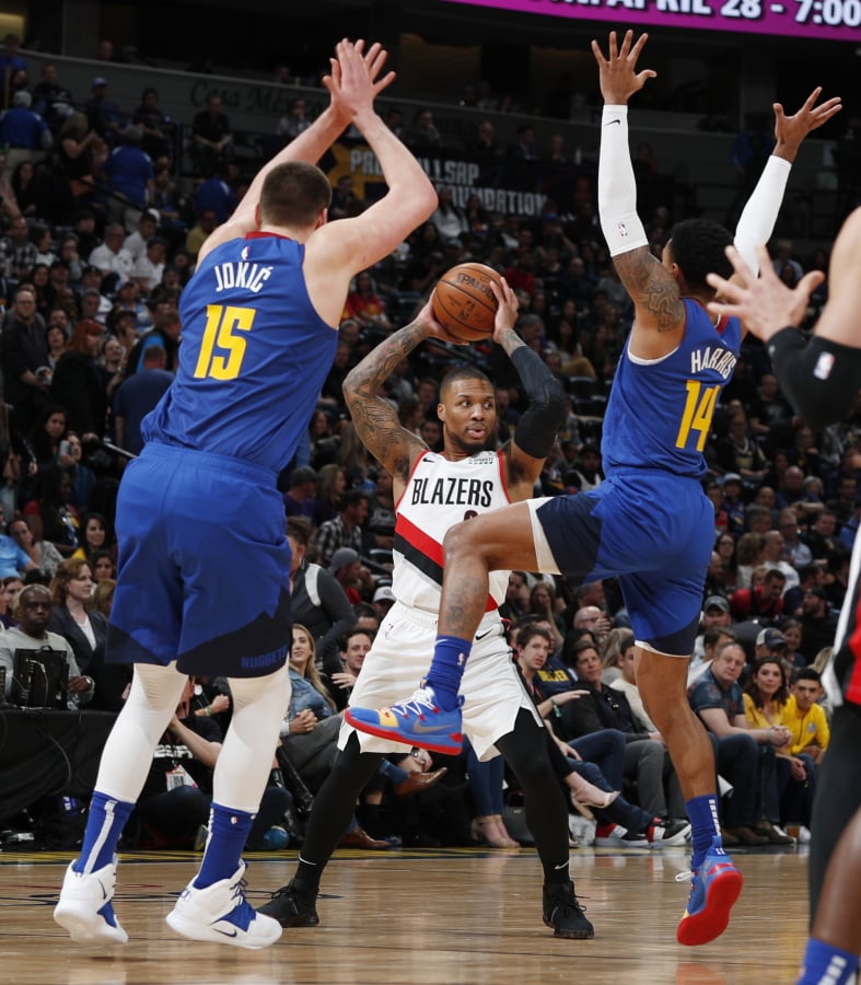 Portland Trail Blazers guard Damian Lillard, rear, looks to pass the ball as Denver Nuggets center Nikola Jokic, left, and guard Gary Harris defend during the second half of an NBA basketball game Friday, April 5, 2019, in Denver. The Nuggets won 119-110.