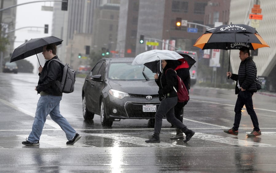 FILE - In this Monday, Feb. 6, 2017 file photo, pedestrians cross a rainy street in downtown Los Angeles. According to a study released in April 2019 in the Bulletin of the American Meteorological Society, even light rain significantly increases the risk of a fatal car crash.