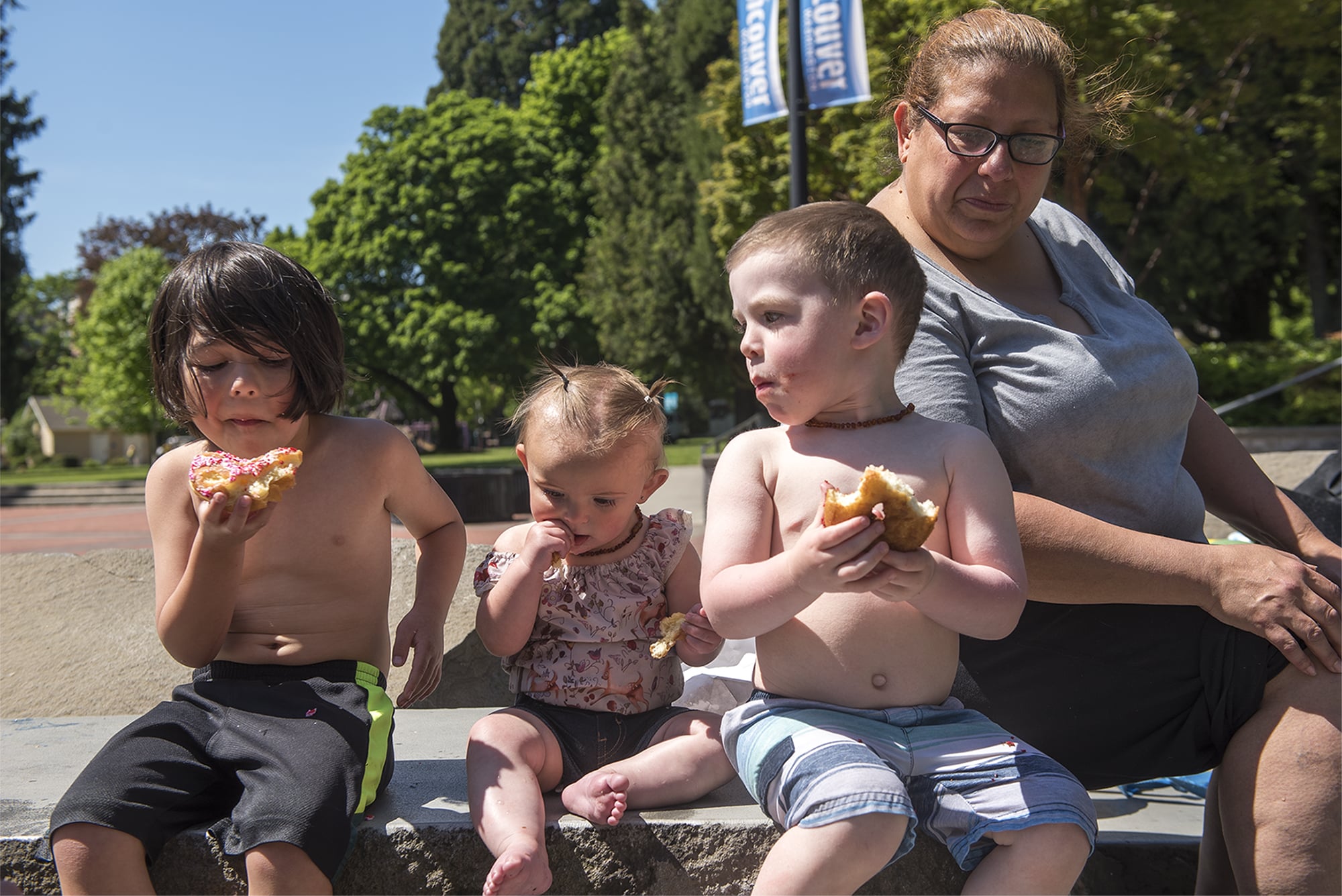 Luka Easterling, 5, from left, Skyler Tumm, 8 months, Logan Tumm, 2, and Brenda Serrano snack on donuts after playing in the water feature in Esther Short Park on Wednesday afternoon, May 8, 2019.