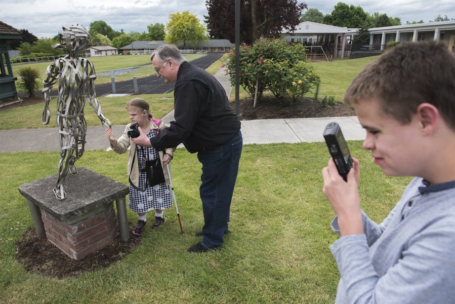 Misty Sahlbom, 16, from left, and Gary Scott examine a statue before taking a photograph of it, while Fenix Roark, 15, composes his own photo of the art installation at the Washington State School for the Blind on Wednesday afternoon. Scott, a longtime photographer, designed a photography program for blind and visually impaired students at the Vancouver campus.