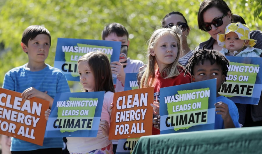 Children hold signs as they stand on stage with Washington Gov. Jay Inslee, who signed bills addressing climate change, Tuesday, May 7, 2019, in Seattle.