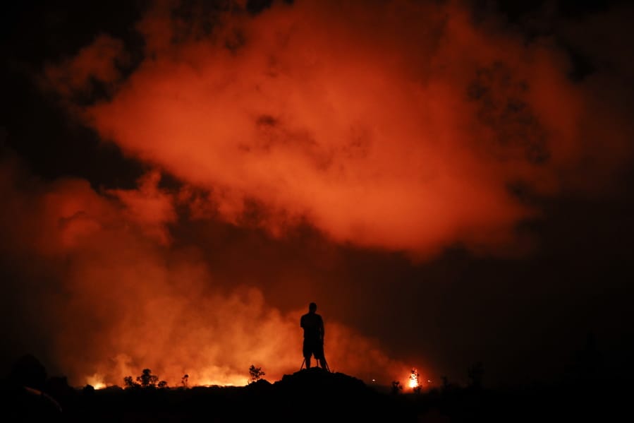 In this Friday, May 18, 2018 file photo, Peter Vance photographs lava erupting in the Leilani Estates subdivision near Pahoa, Hawaii. A year after one of Kilauea volcano’s largest and most destructive eruptions, people who lost their Big Island homes and farms to rivers of lava are still struggling to regain a sense of normalcy. More than 700 homes were destroyed in the historic eruption, and most people will never move back to their land. (AP Photo/Jae C.