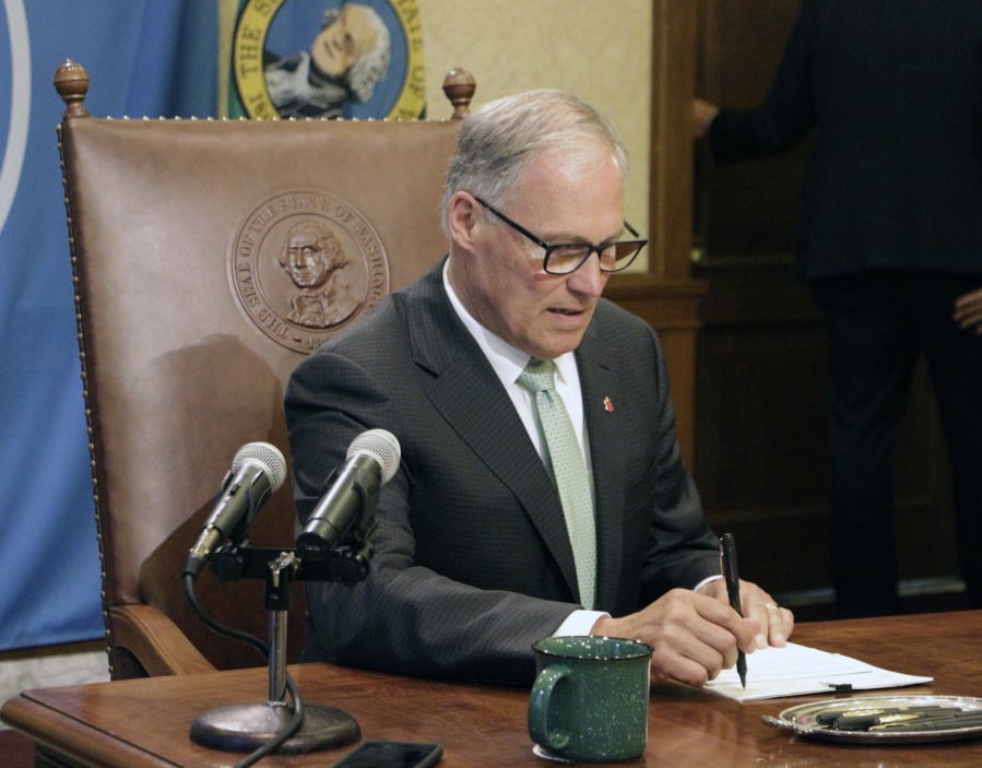 Washington Gov. Jay Inslee looks at one of a slate of bills designed to help the Pacific Northwest’s endangered orcas on Wednesday, May 8, 2019, in Olympia, Wash. The measures include requiring more oil shipments to have tugboat escorts to prevent spills, allowing anglers to catch more walleye and bass that prey on young salmon, and giving state agencies the authority to ban toxic chemicals in consumer goods.