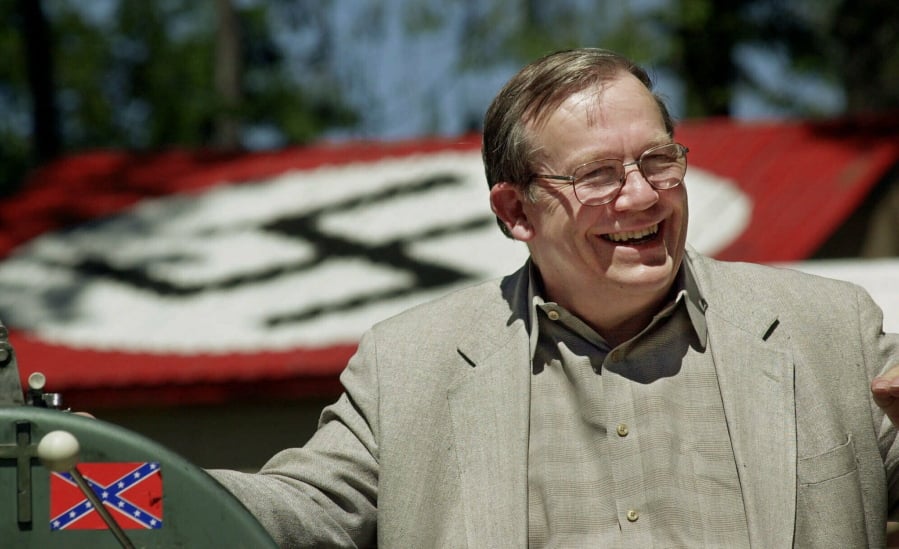 FILE - In this May 22, 2001, file photo, Norm Gissel smiles as he talks about the imminent dismantling of the former headquarters of the Aryan Nations in Hayden Lake, Idaho. Behind Gisel is a Nazi insignia painted atop the roof of the compound’s cafeteria. Nearly two decades after the Aryan Nations compound was demolished in Idaho, far-right extremists are maintaining a presence in the Pacific Northwest.