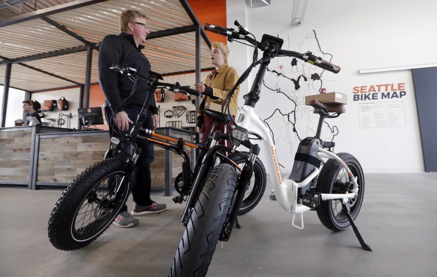 In this photo taken Wednesday, May 15, 2019, customer Torre Treece, left, talks with Rad Power Bikes sales associate Becs Richards about the two electric bikes he bought at the shop in Seattle. The bicycle company said that they will absorb 100% of any tariff on their Chinese-made bicycles.