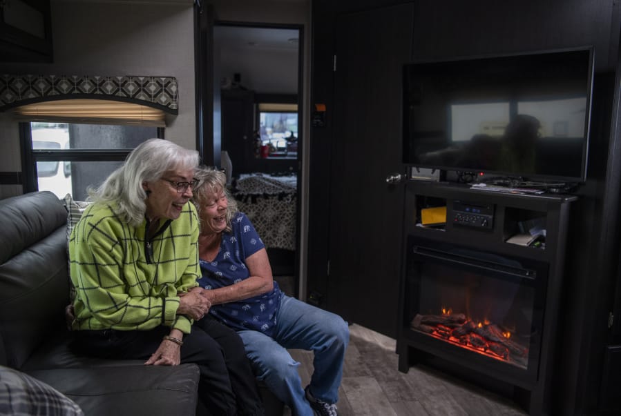 Edith Perrone, left, and her daughter, Glenda Peck, enjoy the electric fireplace in Perrone’s new trailer. As rent prices increased, Peck decided to buy a 26-foot recreational vehicle and move into a park. Her mother followed suit a few years later, putting her large family home on the market and purchasing a new 37-foot trailer.