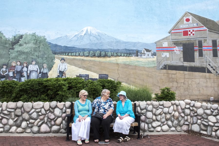 Sharon York, from left, Dianne Underwood and Patricia Buzzini talk while sitting in front of a mural featuring their family at Orchards Plaza.