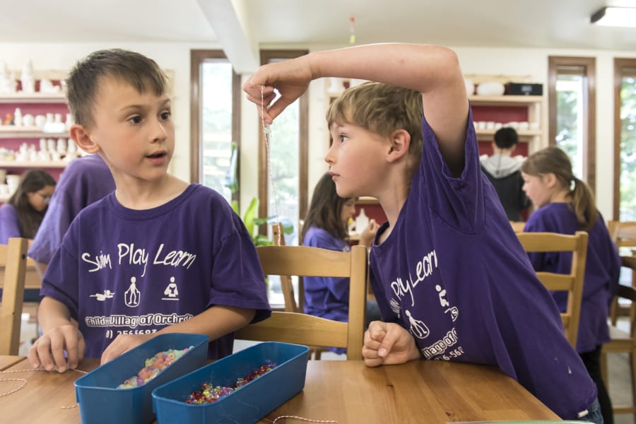 Lincoln Carballo, 7, left, listens as Connor Baldwin explains how to tie a knot at Earth, Glaze and Fire while visiting the shop as part of their Children’s Village of Orchards Daycare summer outing.