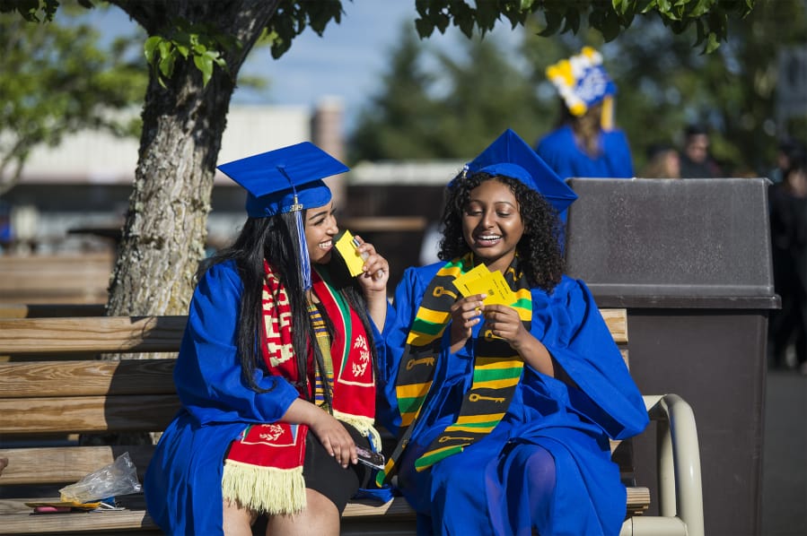Milkana Ghebretensae, left, and Abesha Kebede share a joke while waiting for the start of the Clark College commencement ceremony at the Sunlight Supply Amphitheater on Thursday night. Both are Running Start students, graduating with both their associate degrees and their high school degrees.