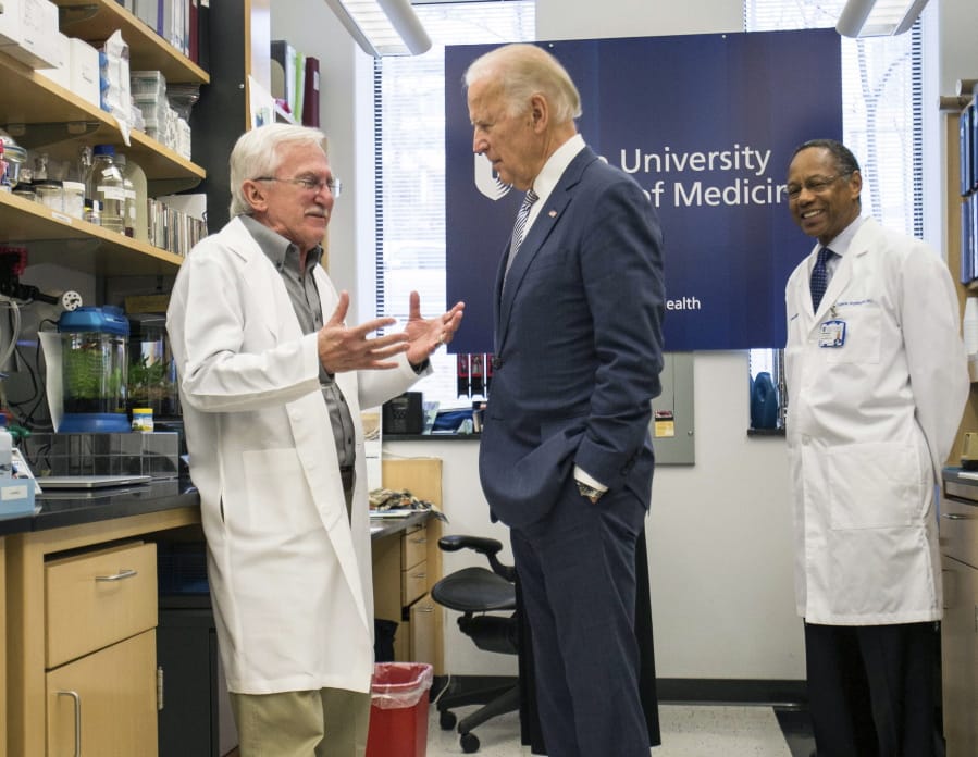 FILE - In this Feb. 10, 2016 file photo, Vice President Joe Biden speaks with Nobel Laureate Dr. Paul Modrich, left, as Dr. A. Eugene Washington, Chancellor for Health Affairs at Duke University, right listens in a laboratory at Duke University School of Medicine in Durham, N.C. Biden’s defining venture since leaving the Obama White House is the Biden Cancer Initiative, a nonprofit aimed at speeding a cancer cure in memory of his son.