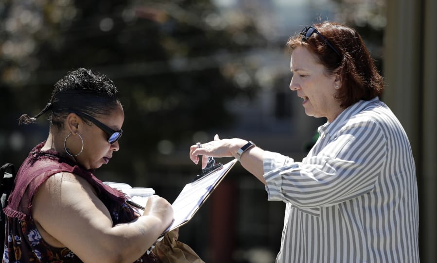 In this photo taken Monday, June 10, 2019, Seattle City Council candidate Pat Murakami, right, looks on as voter Lashaun Hartfield signs a replacement voucher for Murakami’s campaign in Seattle. A first-of-its-kind public campaign finance program in Seattle gives voters vouchers worth $100 to pass on to any candidate they want. Now in its second election cycle, advocates say the program can level the political playing field, although its first round in Seattle showed mixed results.