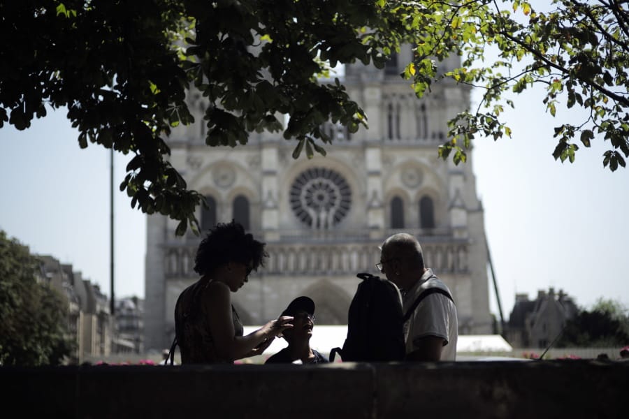 Tourists chat under a tree in front of Notre Dame Cathedral, Wednesday, June 26, 2019 in Paris. High temperatures are expected to go up to 39 degrees Celsius (102 Fahrenheit) in the Paris area later this week and bake much of the country, from the Pyrenees in the southwest to the German border in the northeast.
