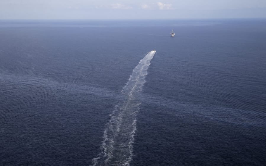 FILE- In this March 31, 2015 aerial photo, the wake of a supply vessel heading towards a working platform crosses over an oil sheen drifting from the site of the former Taylor Energy oil rig in the Gulf of Mexico, off the coast of Louisiana. A new federally led estimate of oil seeping from a platform toppled off Louisiana 14½ years ago is below other recent estimates. But the report contradicts the well owner’s assertions about the amount and source of oil. Oil and gas have been leaking into the Gulf of Mexico since a subsea mudslide caused by Hurricane Ivan on Sept. 15, 2004 knocked over a Taylor Energy Co. production platform.