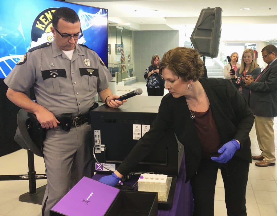 FILE - In this April 10, 2019, file photo, Regina Wells, foreground right, a forensic laboratories supervisor with the Kentucky State Police, demonstrates new crime-fighting technology in Frankfort, Ky. Rapid DNA machines roughly the size of an office printer have helped solve rape cases in Kentucky. Now a state board in Texas has asked a growing government provider of the DNA equipment used in those high-profile projects to halt work amid concerns of potentially jeopardized criminal cases, according to a letter obtained by The Associated Press.