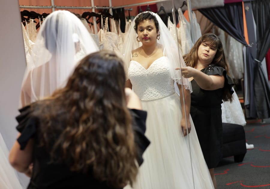 Ann Campeau, right, owner of Strut Bridal, fits a new dress on inventory manager Stefanie Zuniga at her shop in Tempe, Ariz.