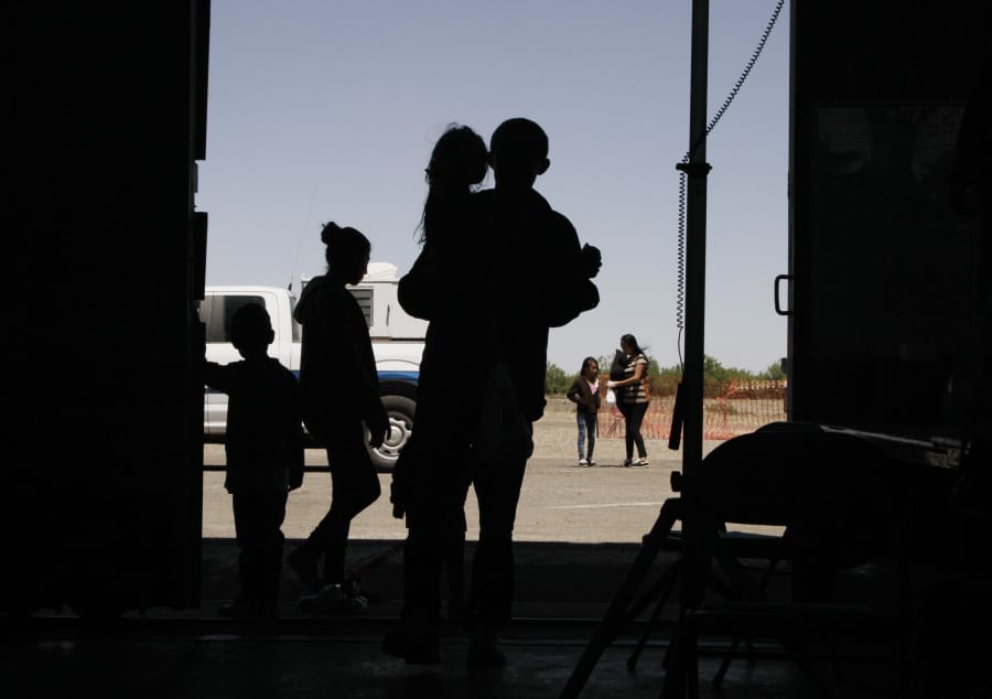 FILE - In this Wednesday, May 22, 2019 file photo migrants mainly from Central America guide their children through the entrance of a World War II-era bomber hanger in Deming, N.M. A panel of appeals court judges in California will hear arguments in the long-running battle between advocates for immigrant children and the U.S. government over conditions in detention and holding facilities near the southwest border.