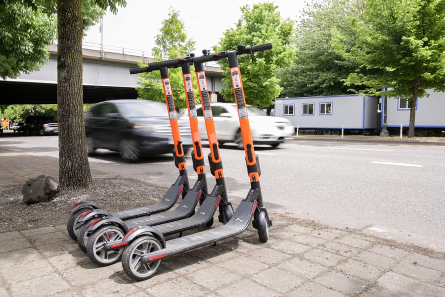 Commuters pass by a row of parked SPIN electric scooters May 17 on Southwest Naito Parkway in downtown Portland.  (Bryan M.