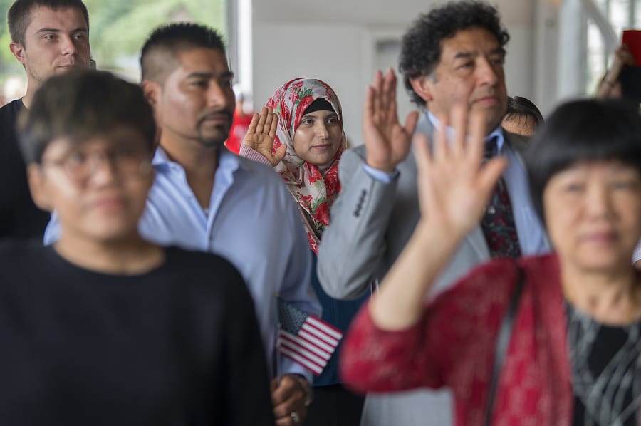 Jalilah Alzeyadi, center, who is originally from Yemen and now lives in Vancouver, joins fellow candidates for citizenship as they take the oath of allegiance during the Special Naturalization Ceremony at the Pearson Air Museum’s historic hangar Wednesday afternoon.