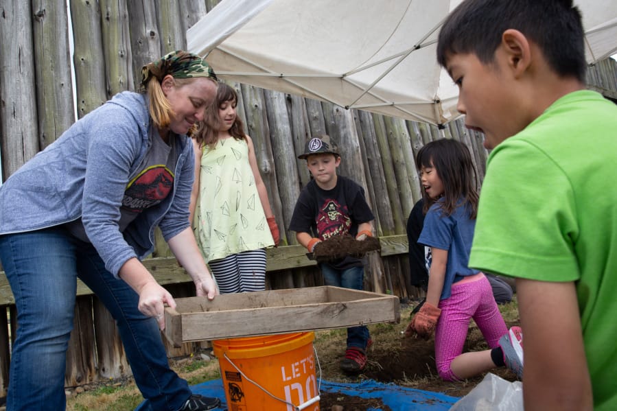 Volunteer Erin Miermans, from left, Evelynn Ramsay, 8, of Vancouver, Rhonin Parks, 8, of Vancouver, Kaitlyn Chan, 6, and her brother, Emlyn Chan, 10, both of Redmond, watch as dirt from the mock archeological dig is sifted Saturday at Fort Vancouver National Historic Site.