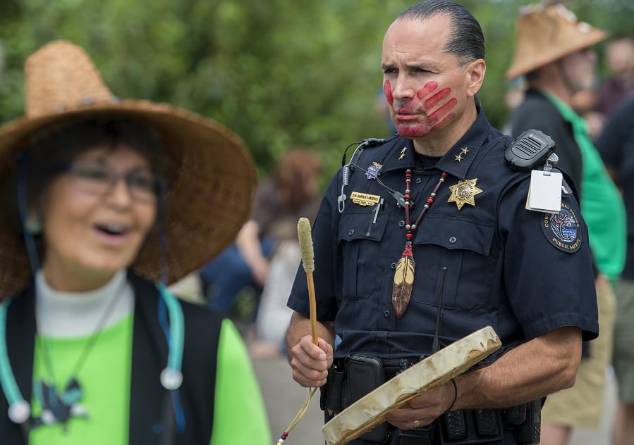 Duane Garvais Lawrence, assistant chief for the tribe’s police department, drums as he waits for canoes to arrive Friday at Marine Park in Vancouver. The red handprint on his face is to raise awareness for missing and murdered indigenous women and girls.