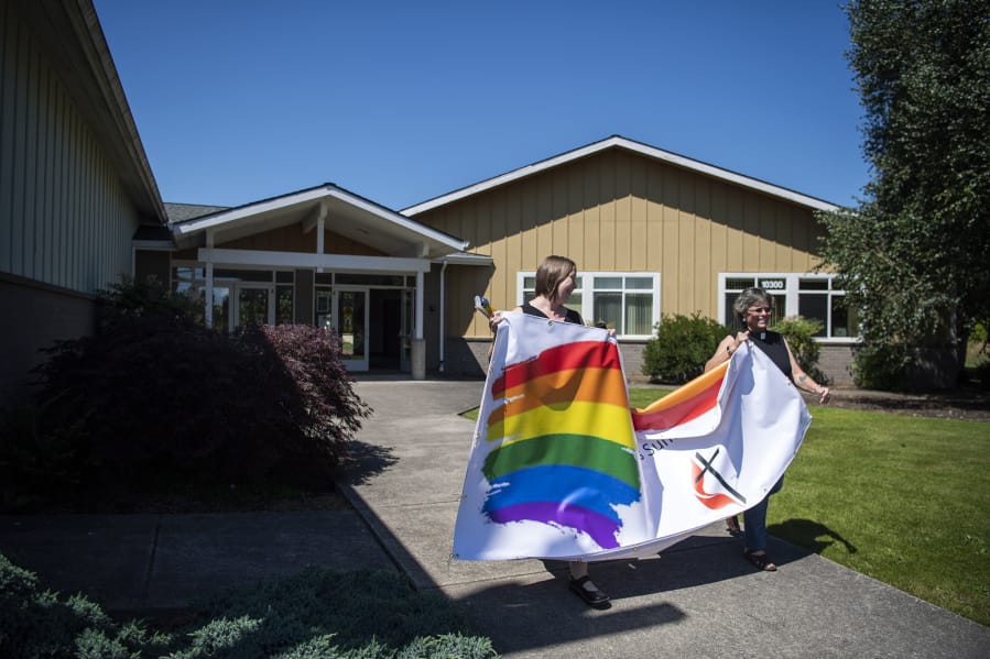 Congregant Kristin Wade, left, and Pastor Susan Boegli, right, carry new welcome banners to the front of the Battle Ground Community United Methodist Church on Northeast 199th Street. Boegli said the church added a rainbow to its sign two years ago to show that all are welcome regardless of sexual orientation. It has been repeatedly vandalized and, as a result, reprinted.