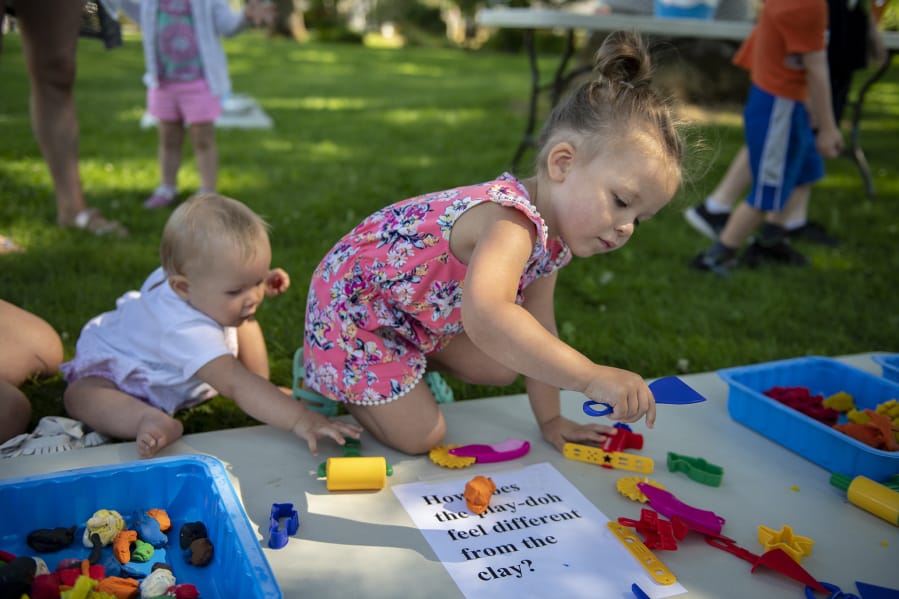Nine-month-old Haddie Gordon, left, and sister Willow, 3, amuse themselves with Play-Doh on Thursday morning outside the Woodland Community Library during its Sensory Play in the Park event. Library staffers hope they will be able to host more activities for kids and families once the Fort Vancouver Regional Library District raises enough money to construct a bigger building in Woodland.