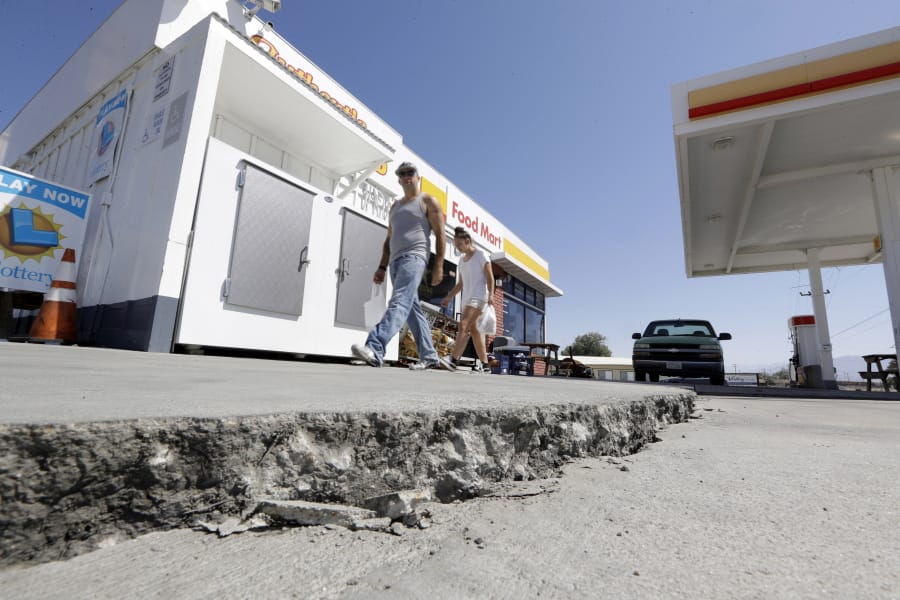 People walk past a crack in a gas station’s driveway July 6 in Trona, Calif.