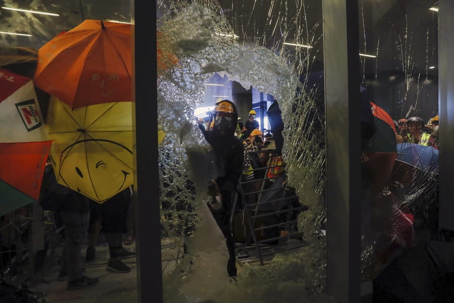 In this file photo taken Monday, July 1, 2019, a protester breaks the glass wall to enter the Legislative Council in Hong Kong, Protesters in Hong Kong took over the legislature’s main building Monday night, tearing down portraits of legislative leaders and spray painting pro-democracy slogans on the walls of the main chamber.