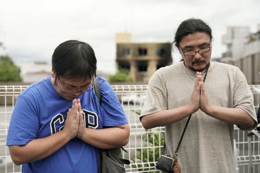 Two men pay respects at a makeshift memorial site to honor the victims of Thursday’s fire at the Kyoto Animation Studio building, background center, Friday, July 19, 2019, in Kyoto, Japan. (AP Photo/Jae C.