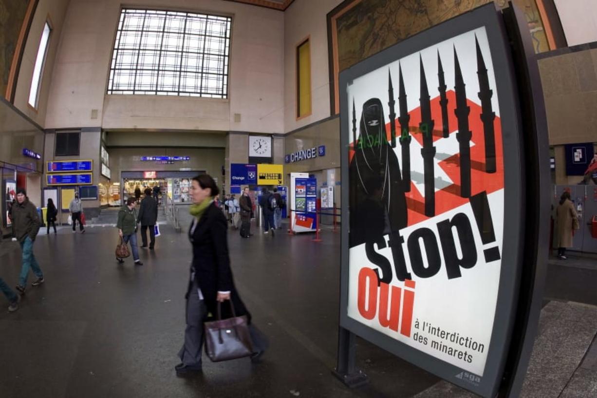 People walk by a poster from the right-wing Swiss People’s Party depicting a woman wearing a burqa in front of a Swiss flag upon which are minarets, which resemble missiles in November 2009 at the central station in Geneva, Switzerland. Later in the month, a successful referendum banned the construction of new minarets in the country.