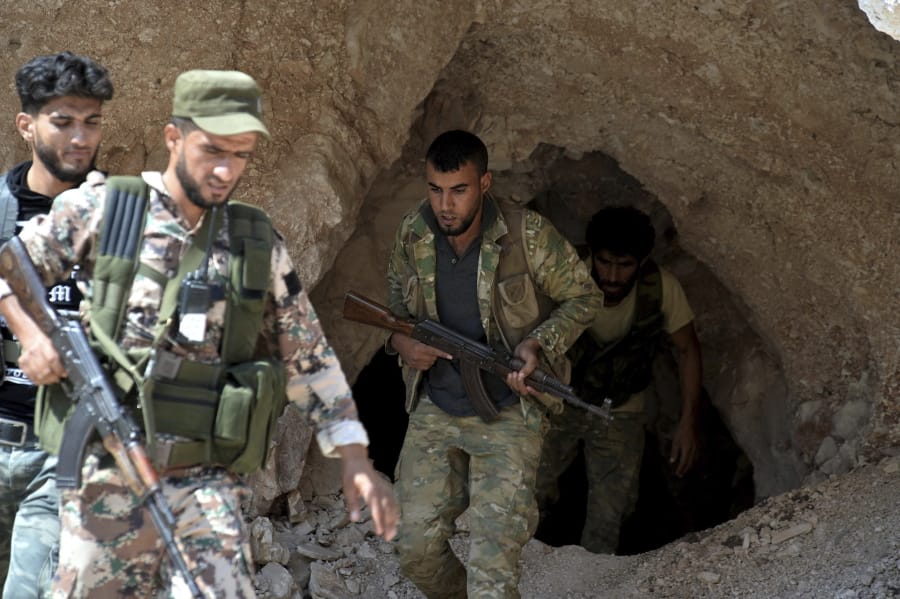 FILE - In this Sept. 9, 2018 file photo, fighters with the Free Syrian army exit a cave where they live, on the outskirts of the northern town of Jisr al-Shughur, west of Idlib, Syria. n two months of intensive airstrikes and bombardments on the rebel-controlled province of Idlib, Syrian government forces and their Russian allies have failed to make progress against battle-hardened insurgents.