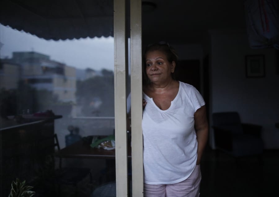 Orelis Lehmann stands on the balcony ‘s door of her dark apartment in Caracas, Venezuela, Tuesday, July 23, 2019. A power outage that began Monday afternoon at the start of rush hour was one more in a series of prolonged blackouts that have unnerved Venezuelans this year and also hit hard the building where Lehmann lives.