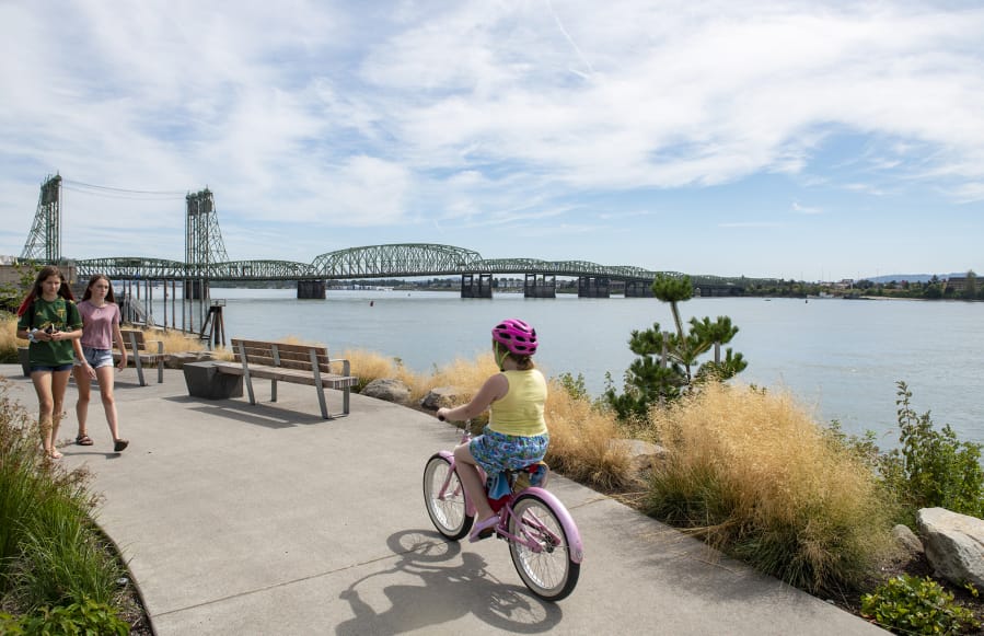 Jaidyn Geesey, left, and Ava Soucy stroll along the Columbia River at Vancouver Waterfront Park on Wednesday afternoon. The Interstate 5 Bridge, which both states want to replace, spans the Columbia River behind them.