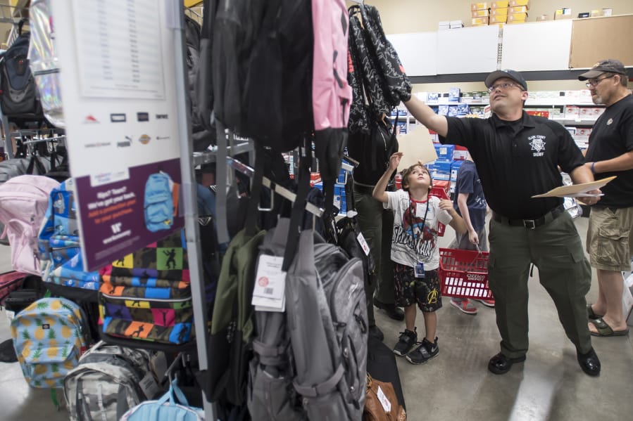 Mitchell Middleton, 6, waits for Clark County sheriff’s Deputy Brad Robinson to grab a backpack from the top rack during Tuesday morning’s Shop with a Cop event at Office Depot in Hazel Dell.