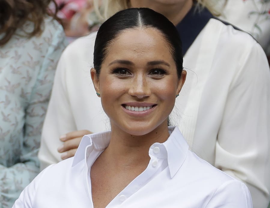 FILE - In this July 13, 2019 file photo, Kate, Meghan, Duchess of Sussex smiles while sitting in the Royal Box on Centre Court to watch the women’s singles final match between Serena Williams, of the United States, and Romania’s Simona Halep on at the Wimbledon Tennis Championships in London. Meghan has guest edited the September issue of British Vogue with the theme “Forces for Change.” Royal officials say the issue coming out Aug. 2 features “change-makers united by their fearlessness in breaking barriers” and includes a conversation between Meghan and former U.S. first lady Michelle Obama.