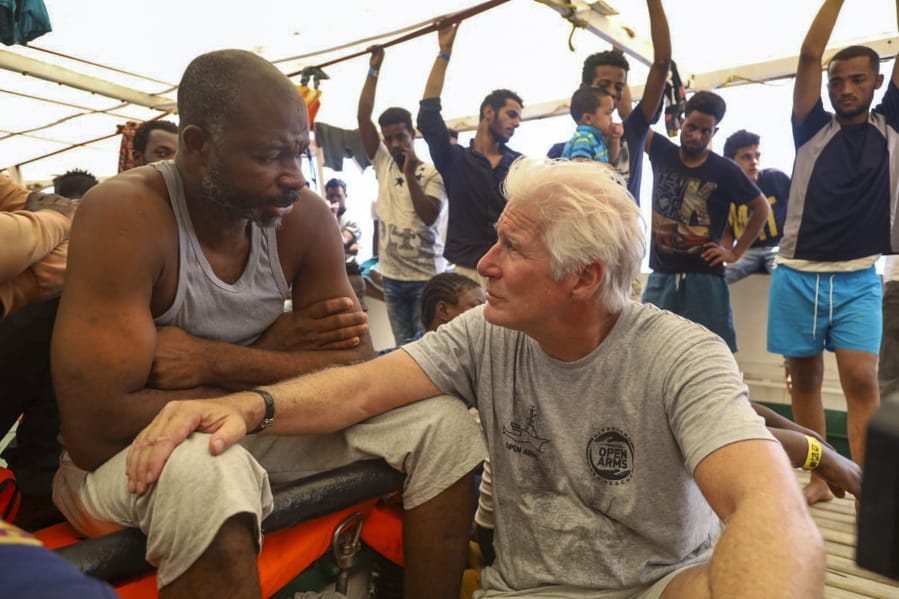 Actor Richard Gere, right, talks with migrants aboard the Open Arms Spanish humanitarian boat as it cruises in the Mediterranean Sea, Friday, Aug. 9, 2019. Open Arms has been carrying 121 migrants for a week in the central Mediterranean awaiting a safe port to dock, after it was denied entry by Italy and Malta.