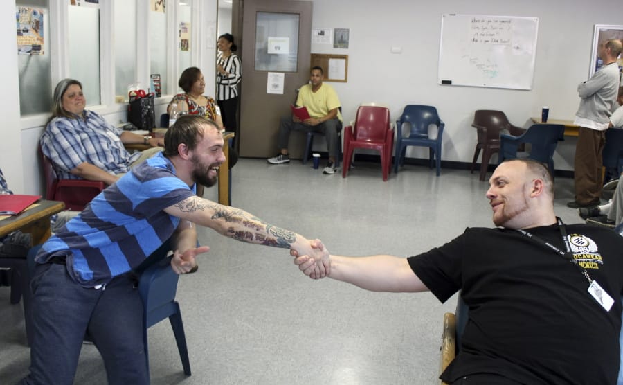 In this Aug. 5, 2019 photo, Israel Rivera, left, and Michael Manning greet each other during a group counseling session at the Hampden County Sheriff's Department's minimum security, residential treatment facility in Springfield, Mass. The county jail is marking one year of treating men civilly committed for substance abuse reasons. Sheriff Thomas Cocchi and his supporters have said the program, one of just three in the state treating civilly committed men and the only in western Massachusetts, can play a key role in efforts to curb the Springfield area's opioid problem. But civil rights group want the practice of imprisoning men for addiction treatment ended.