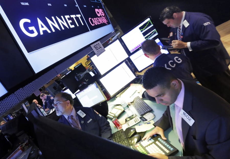FILE - In this Aug. 5, 2014, file photo, specialist Michael Cacace, foreground right, works at the post that handles Gannett on the floor of the New York Stock Exchange. Just a week after announcing its $1.4 billion acquisition of Gannett, GateHouse Media is again laying off journalists and other workers at its newspapers, possibly foreshadowing the future awaiting employees of what will become the largest U.S. newspaper company. GateHouse and Gannett say the merger will allow GateHouse to accelerate the “digital transformation” of its newspapers while paying down huge sums GateHouse borrowed in order to fund the acquisition.