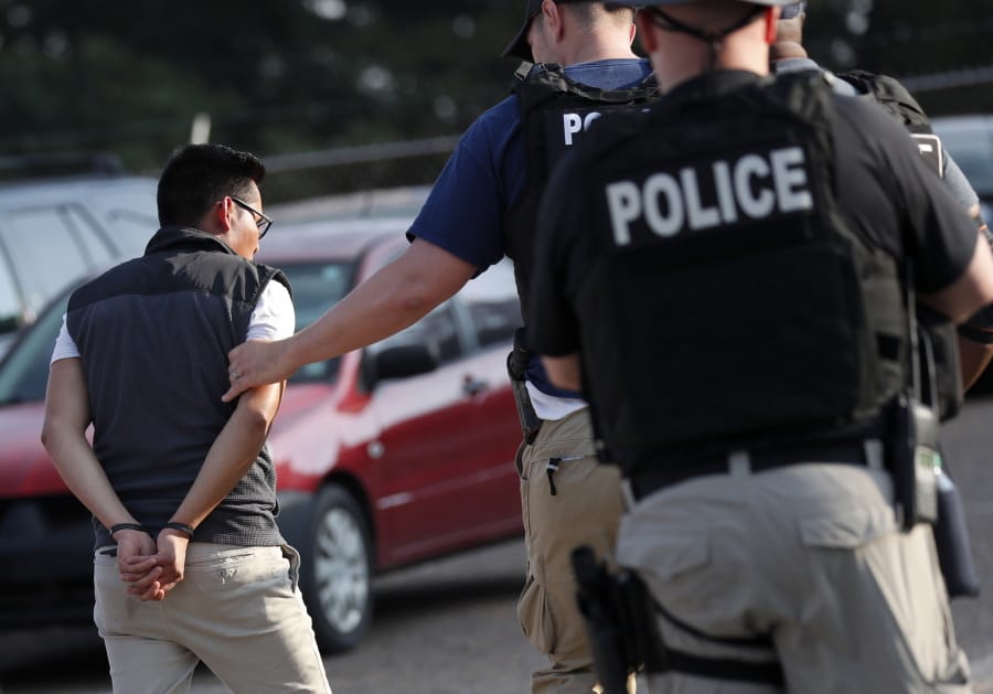 FILE - In this Aug. 7, 2019, file photo, a man is taken into custody at a Koch Foods Inc. plant in Morton, Miss. Unauthorized workers are jailed or deported, while the managers and business owners who profit from their labor often aren’t. Under President Donald Trump, the numbers of owners and managers facing criminal charges for employing unauthorized workers have stayed almost the same. (AP Photo/Rogelio V.