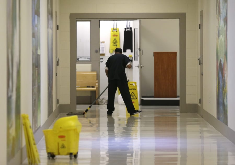FILE - In this June 21, 2017, file photo, a detainee mops a floor in a hallway of the Northwest Detention Center in Tacoma, Wash., during a media tour of the facility.  (AP Photo/Ted S.