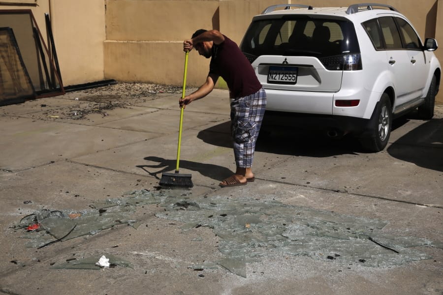 A man sweeps broken glass Sunday near the 11th-floor building that houses the media office in a stronghold of the Lebanese Hezbollah group, in a southern suburb of Beirut, Lebanon.