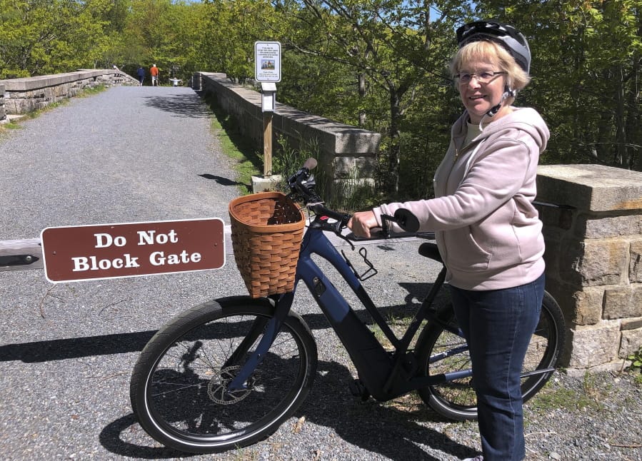 FILE-In this June 8, 2019 file photo, Janice Goodwin stands by her electric-assist bicycle at a gate near the start of the carriage path system where bikes such as her are banned inside Acadia National Park, in this photo June 8, 2018, in Bar Harbor, Maine.