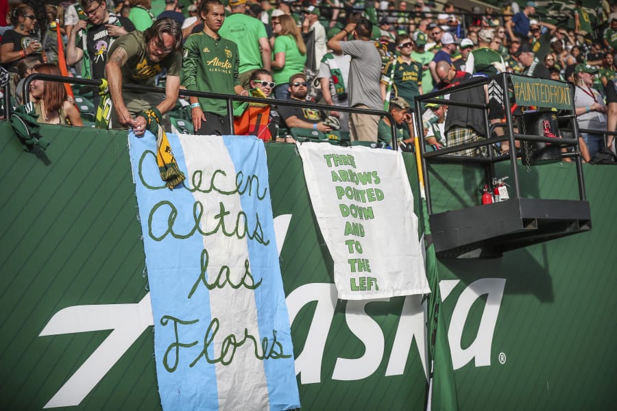 Portland Timbers fans display signs at an MLS soccer match against the Seattle Sounders in Portland on Aug. 23, 2019.. MLS is lifting its ban on signs and banners featuring an anti-Nazi symbol for the remainder of the season and the playoffs. A handful of fans in Portland were prohibited from attending matches this season after challenging a ban on the Iron Front.