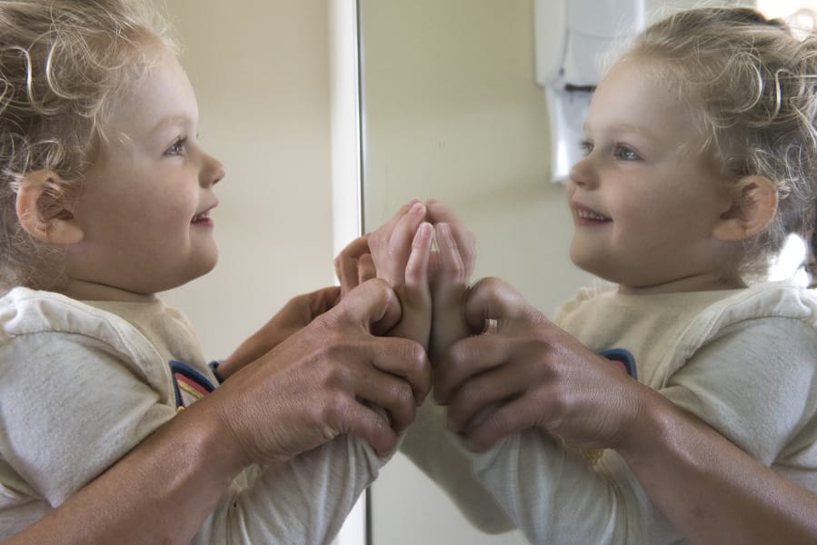 Daphne Calvert, 3, who has Rett syndrome, smiles as physical therapist Amy Scott pushes their hands against a mirror during a therapy session at Legacy Salmon Creek Medical Center in Vancouver. Rett is a rare neurological disorder that causes severe impairments.