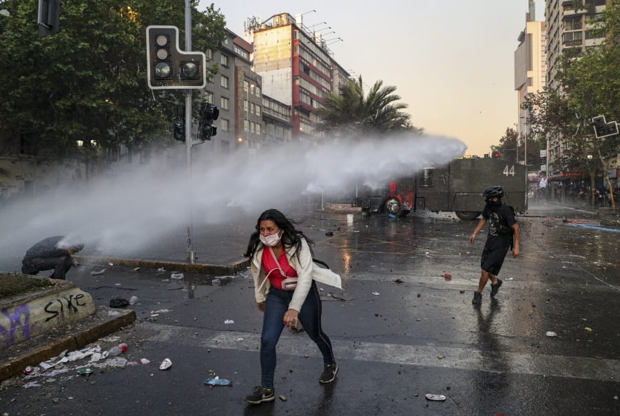 An anti-government protester walks away from the spray of a police water cannon in Santiago, Chile, Tuesday, Oct. 29, 2019. Tuesday is the 12th day of demonstrations that began with youth protests over a subway fare hike that transformed into a leaderless national movement demanding greater equality and better public services in a country long seen as an economic success story.